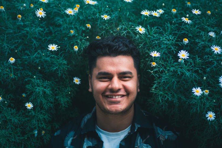 Portrait of smiling young man standing against flowering plants