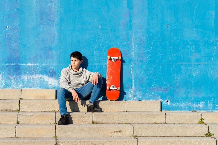 Serious teen sitting on skatepark ramp with a skateboard, looking away