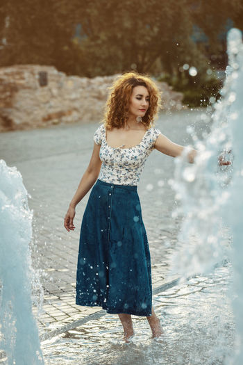 Youn moroccan woman, with curly brown hair, wearing a jean skirt, playing with water at a fountain