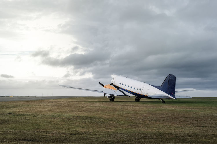 Abandoned airplane on field against cloudy sky