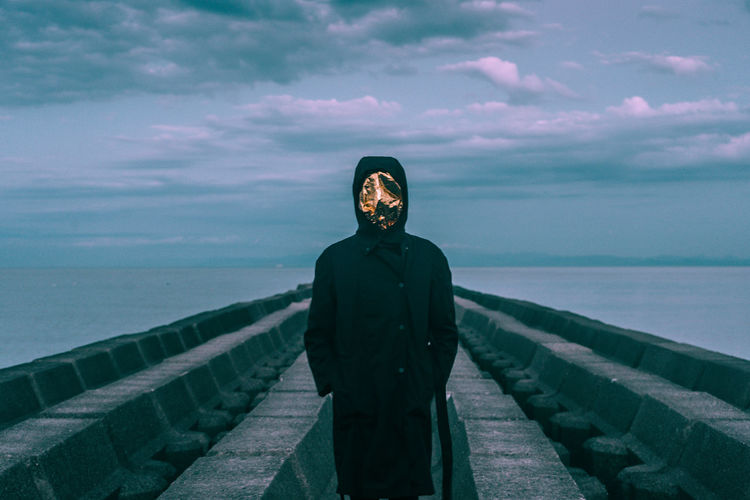 Man wearing mask while standing against sea and sky