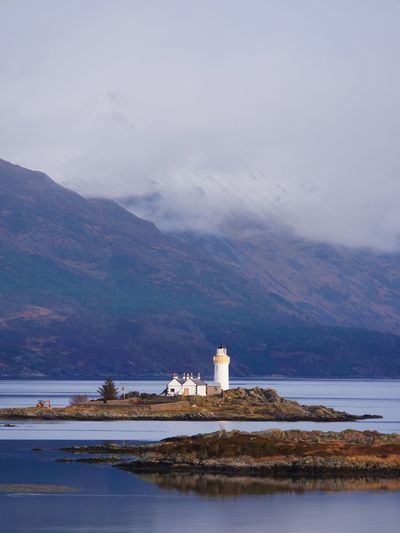 Famous isle ornsay with lighthouse tower, isle of skye, scotland, uk. snowy mountains in background.