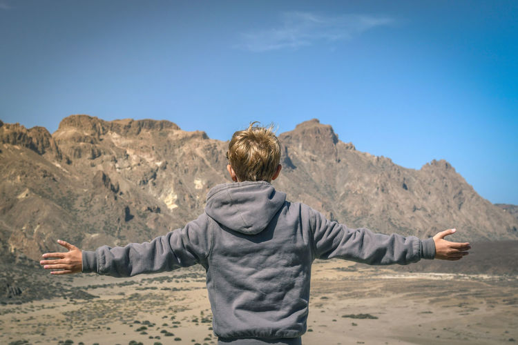 Rear view of boy with arms outstretched standing against mountain