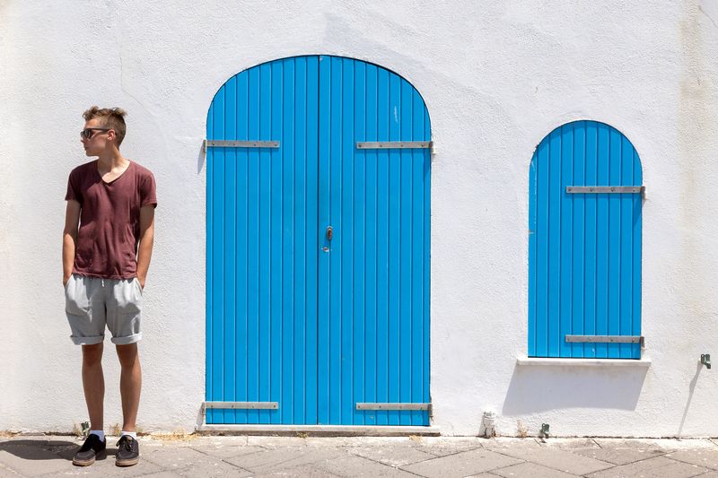 Young man standing next to closed blue door of building