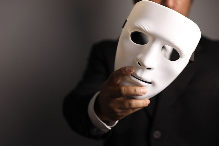 Midsection of man holding mask against gray background