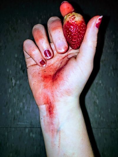 Close-up of bloody hand holding strawberry against wall
