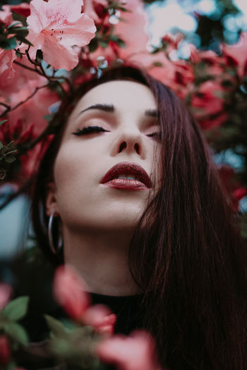 Portrait of a young brunette woman with closed eyes and red lips in spring flowers