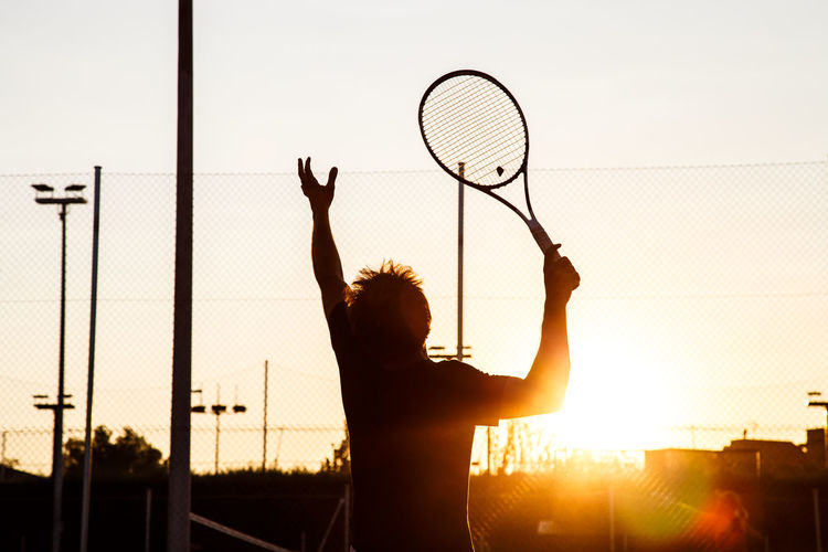 Silhouette man standing by basketball court against sky during sunset