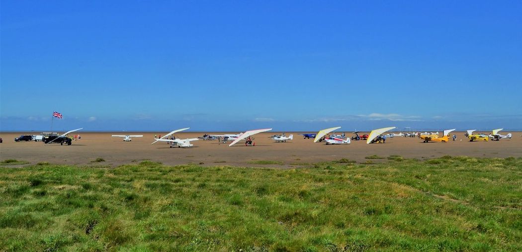 Multiple light aircraft on a beach against blue sky
