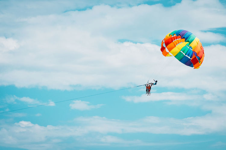 Low angle view of people paragliding against sky