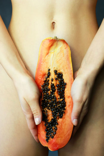 Midsection of naked woman holding halved papaya