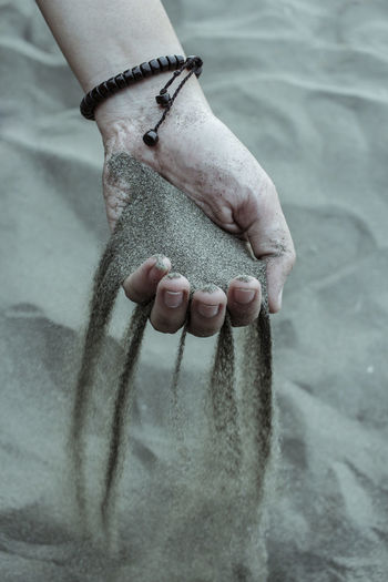Cropped hand of woman spilling sand at beach