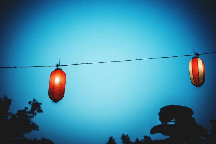 Low angle view of illuminated lanterns against clear blue sky