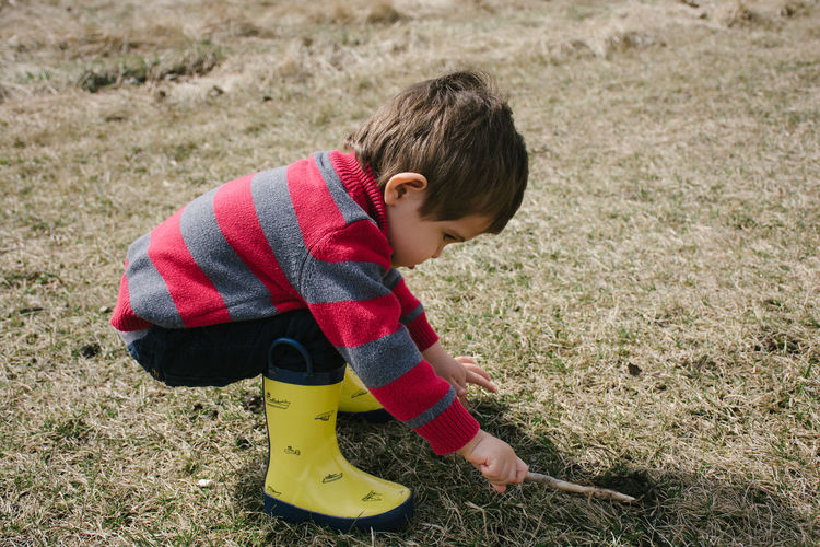 Full length side view of boy playing with stick on grassy field