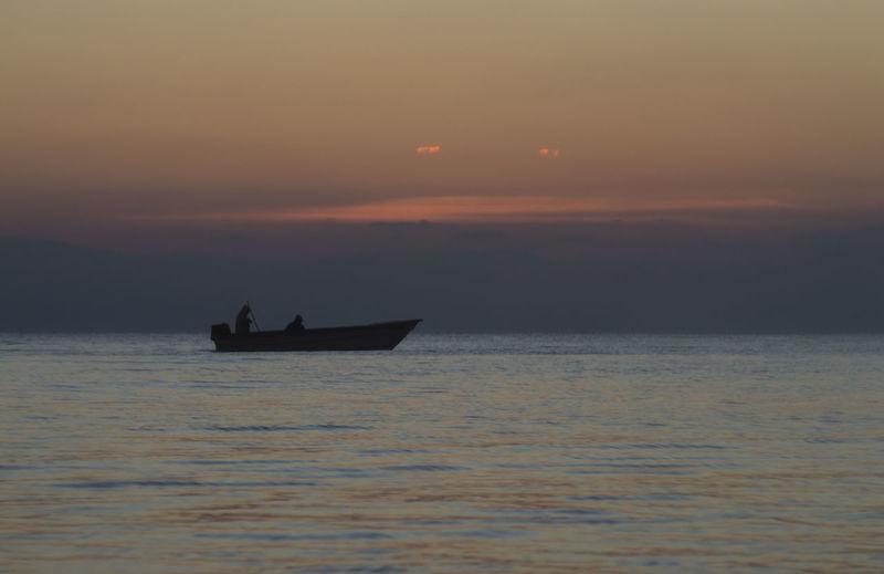 Silhouette boat sailing on sea against sky during sunset