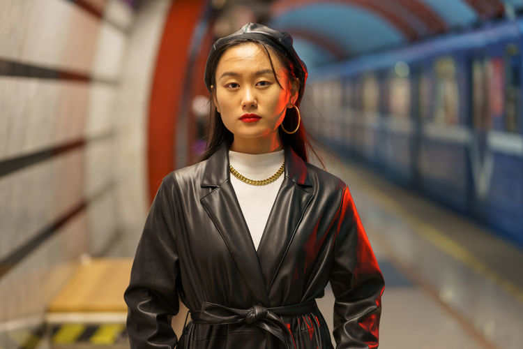Stylish asian girl in leather beret and trench coat wait for train at underground metro station