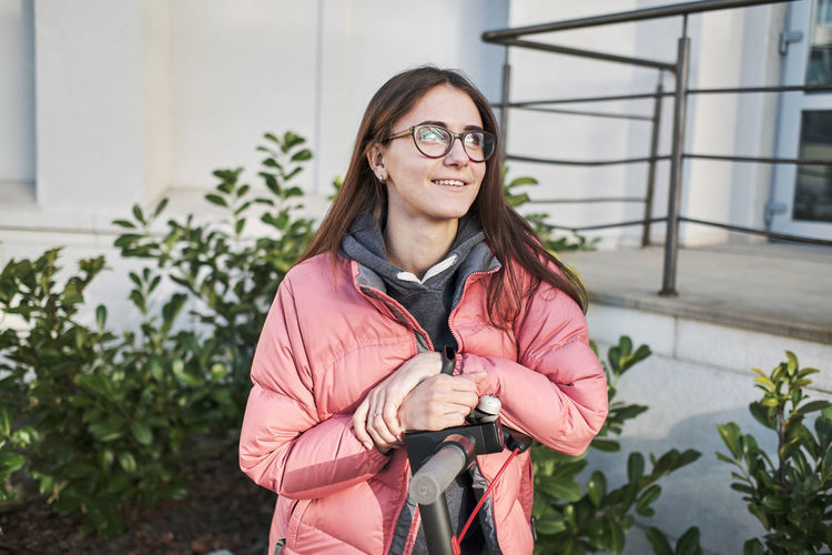 Millennial young girl in a pink jacket on an electric scooter