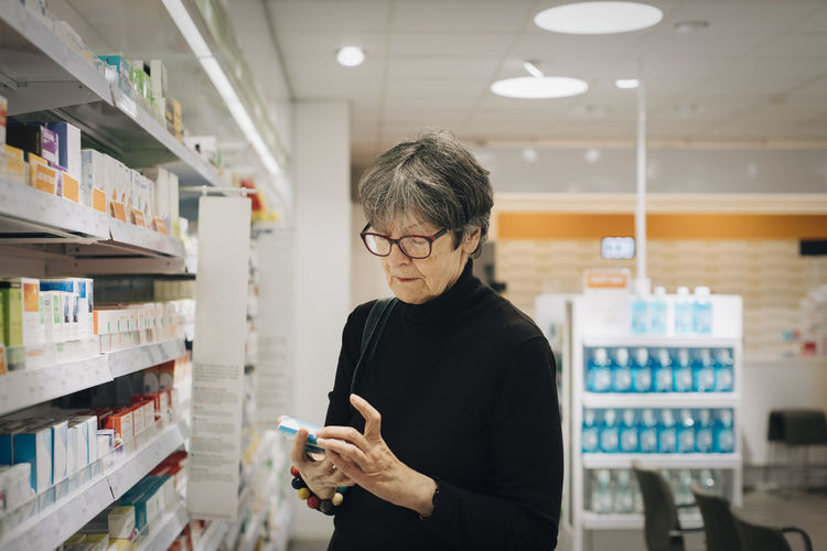 Senior female customer checking medicine by rack at pharmacy store