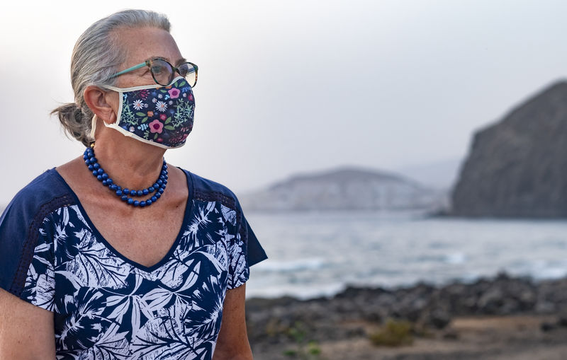 Close-up of senior woman looking away standing against sea