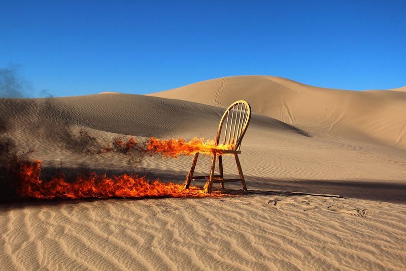 Burning chair in desert against clear blue sky