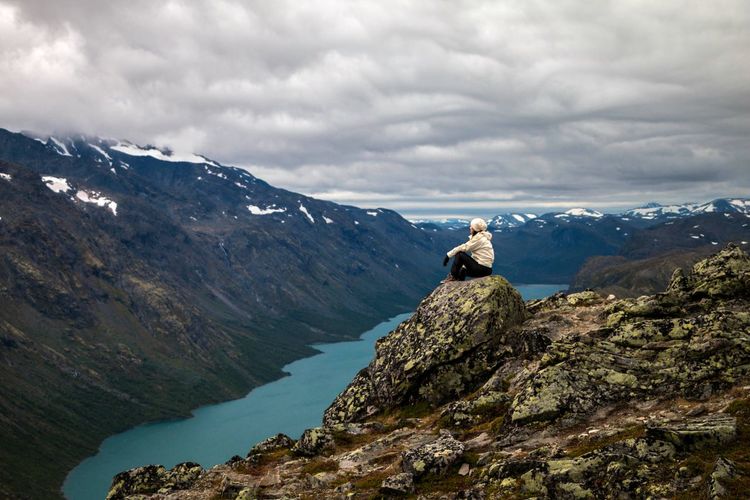 Man sitting on rock by mountains against sky