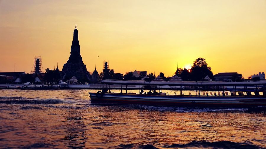 Boat sailing on river chao phraya against wat arun during sunset