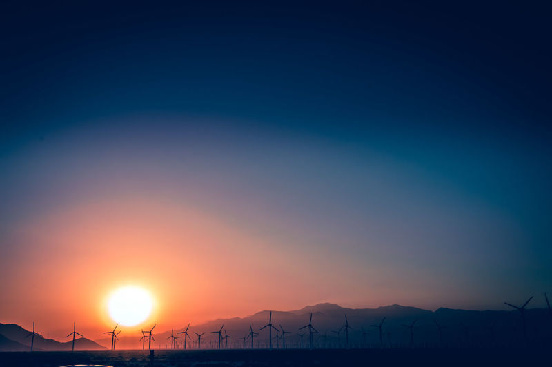 Scenic view of silhouette mountains and windmills against sky during sunset