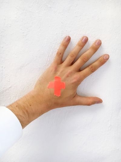 Cropped hand of man with red cross against white wall