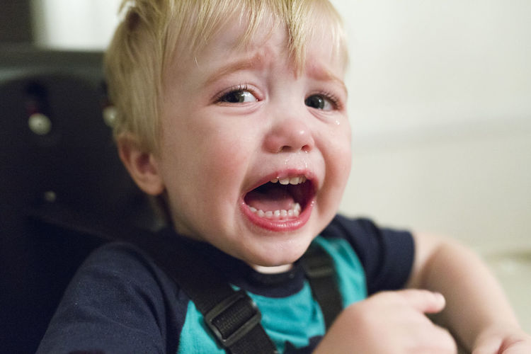 Close-up portrait of angry baby boy crying while sitting on high chair at home