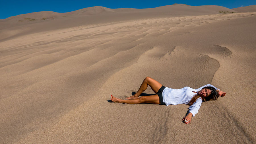 Full length of young woman lying on sand at desert