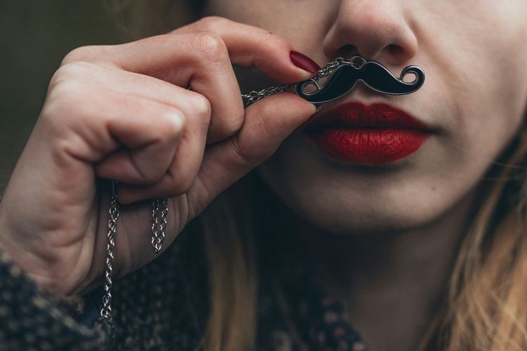 Close-up of young woman holding mustache pattern pendant