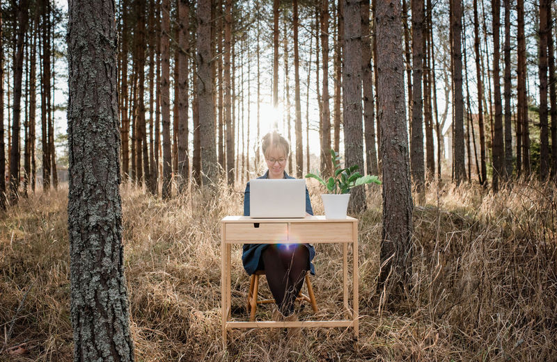 Travelling woman working on a laptop and desk in a peaceful forest