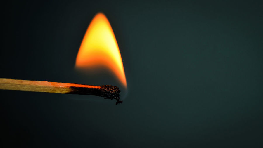 Close-up of burning matchstick over gray background
