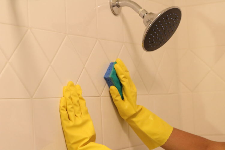 Cropped hands of woman cleaning wall in bathroom