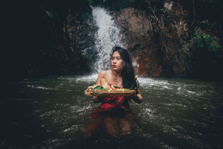 Young woman holding food in wicker basket against waterfall
