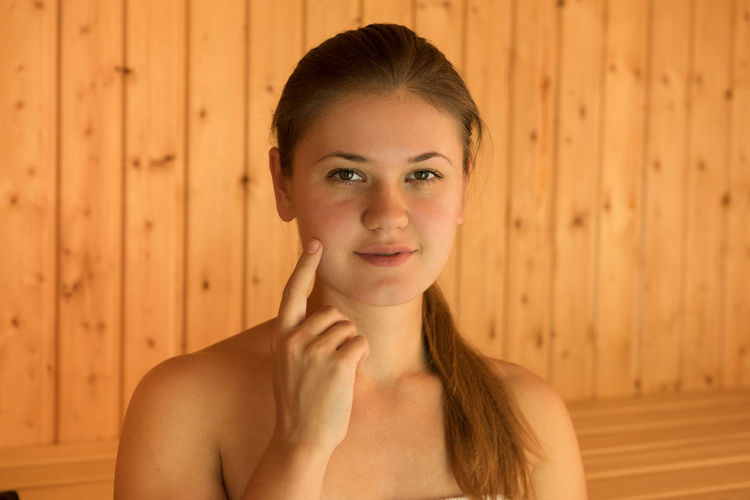 Portrait of beautiful young woman touching face while sitting in sauna