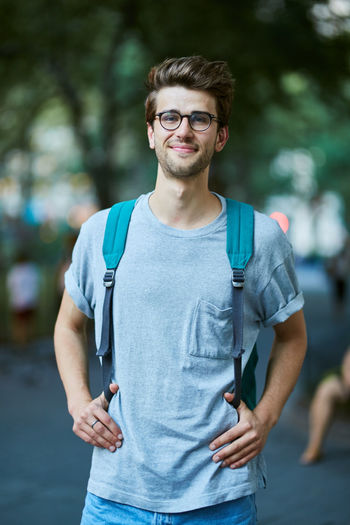 Portrait of young man with backpack standing at park