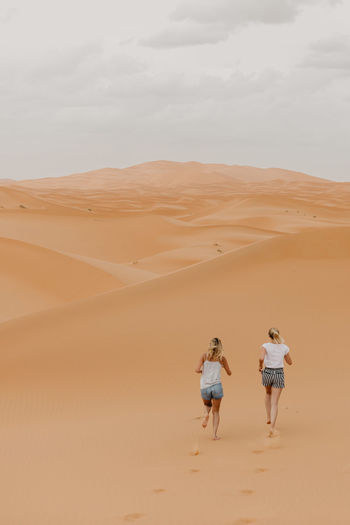 People walking on sand dune in desert against sky
