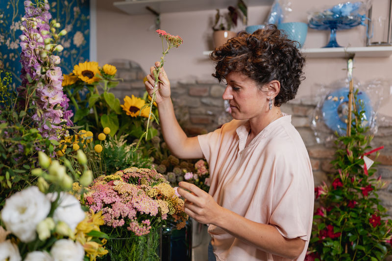 Side view of female florist creating flower bouquet while working at table in floral store