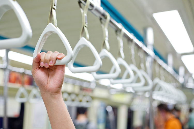 Cropped hand of person holding handle hanging in train