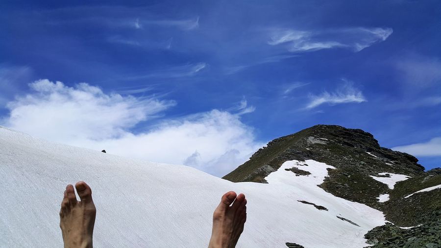 Low section of person on snowcapped mountain against sky