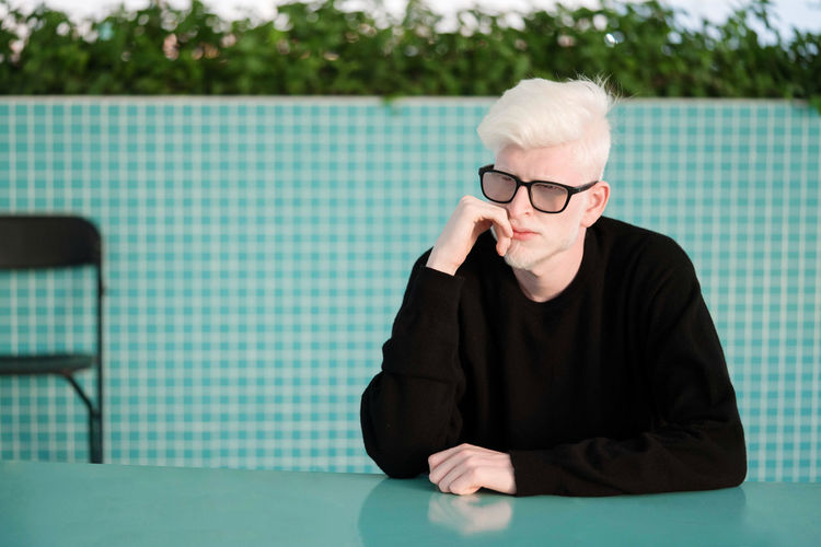 Portrait of the albino man sitting at the blue table thinking