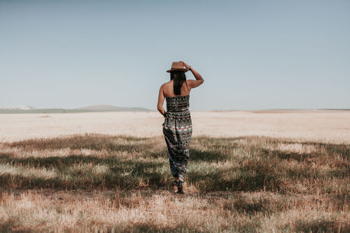 Rear view of woman walking on field against clear sky