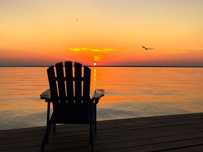 Empty chair on boardwalk at lake during sunrise