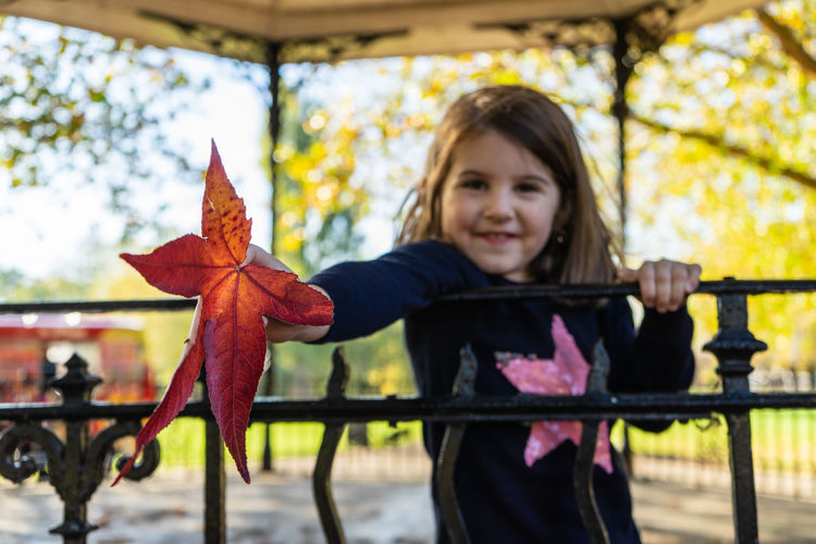 Portrait of smiling girl holding maple leaf during autumn