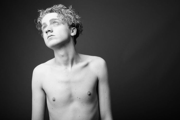Portrait of shirtless man looking away against black background