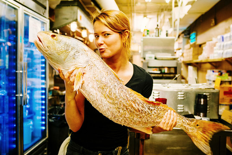 Portrait of young woman holding fish standing at store