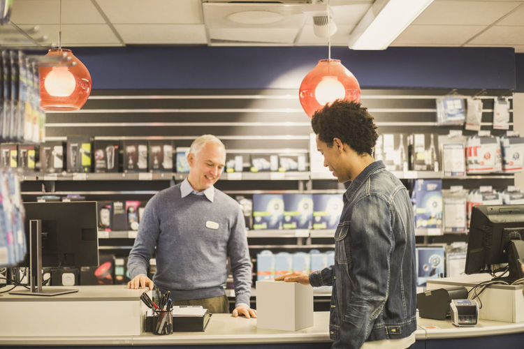 Male customer with kettle box talking to mature owner while standing in electronics store