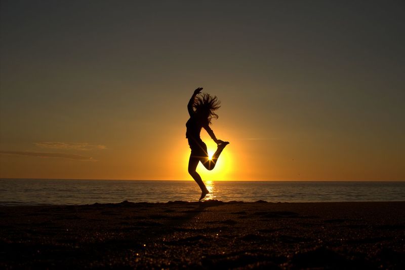 Silhouette of young woman dancing on beach