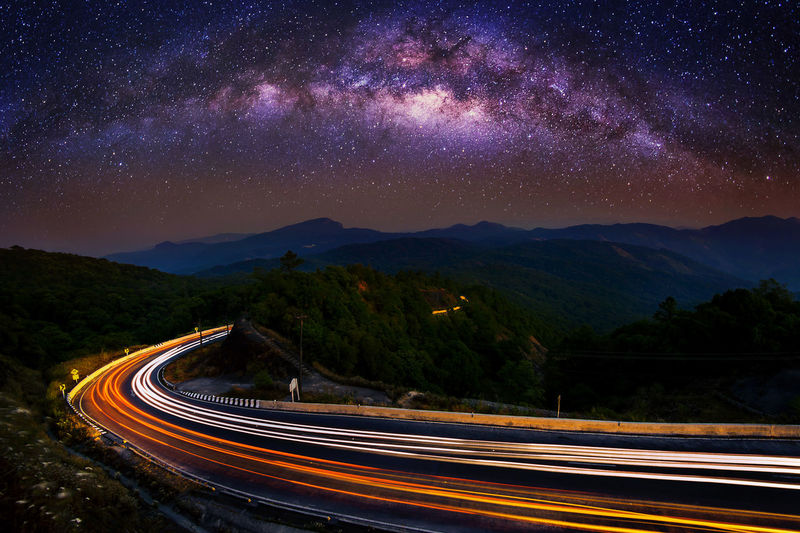 Light trails on road by mountains against sky at night